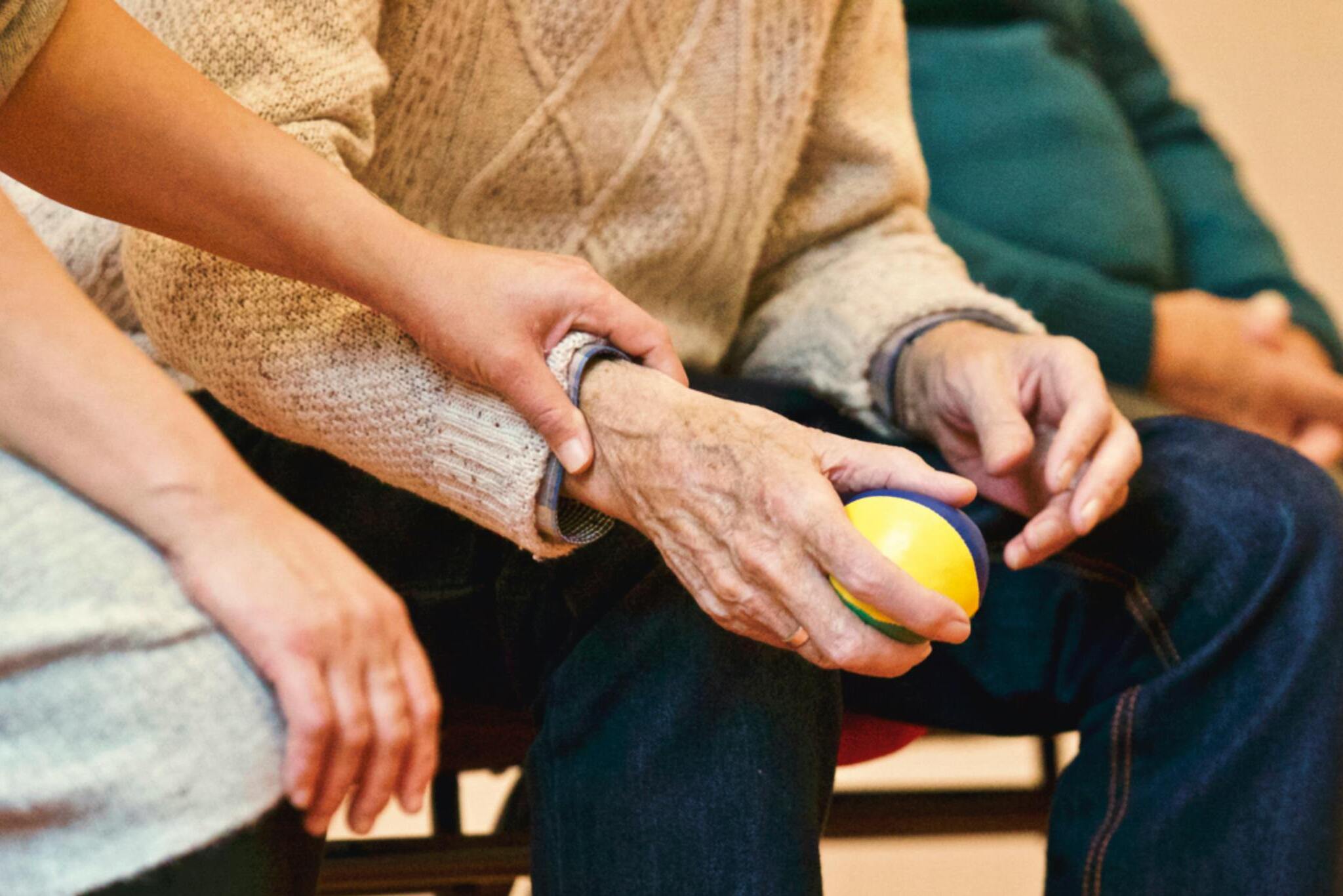 En hjelpepleier holder hånden til en eldre mann som holder en stressball